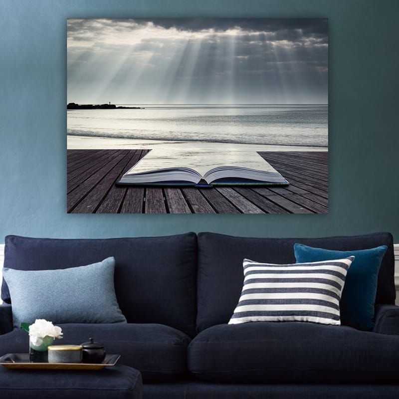 Canvastavla 70x100 cm - Öppen bok som ligger på en träbrygga vid havet, omgiven av mjuka ljusstrålar från en molnig himmel - Grå / Blå / Vit - Inredning - Tavlor & konst - Canvastavlor