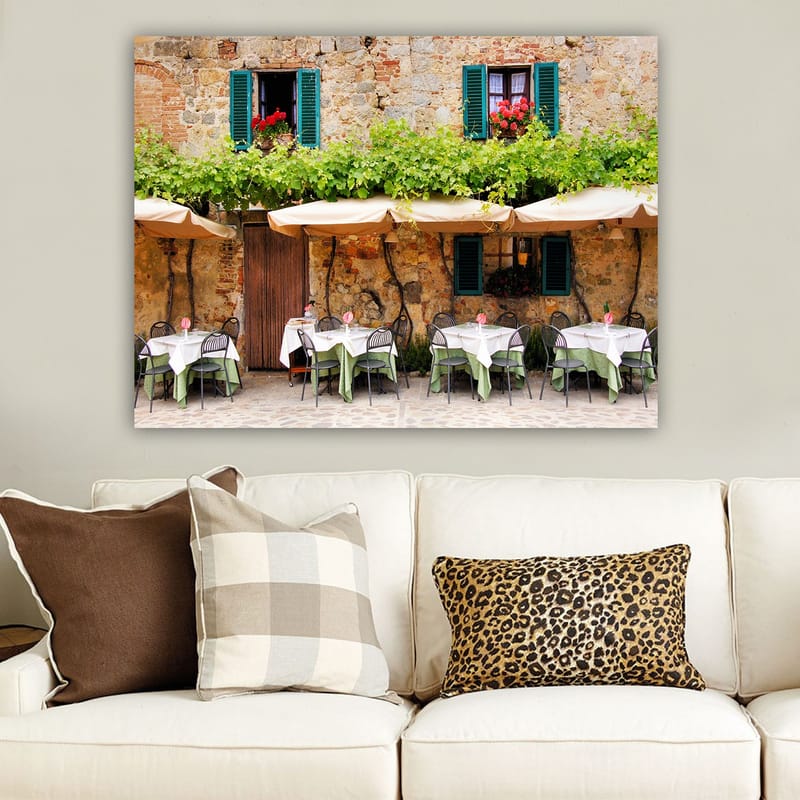 Canvastavla 70x100 cm - Charmig uteservering med vita bord och gröna dukar framför en gammal stenbyggnad med fönsterluckor i mörkgrön färg - Mörkgrön / Vit / Tegelröd - Inredning - Tavlor & konst - Canvastavlor