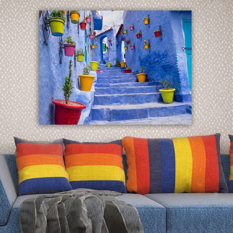 Canvastavla 70x100 cm - Färgglad trappa omgiven av blomkrukor i en pittoresk, blå stadsmiljö - Blå / Gul / Röd - Inredning - Tavlor & konst - Canvastavlor