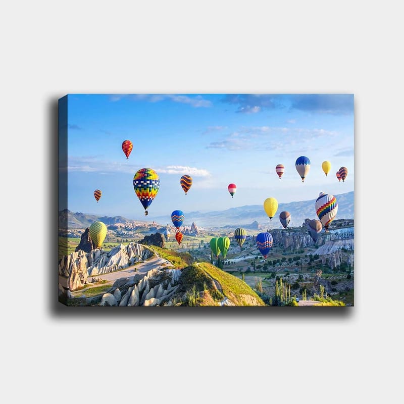 Canvastavla 70x100 cm - Färgglada varmluftsballonger sväva över en vacker landskapsscen i Cappadocia, Grön / Blå / Gul