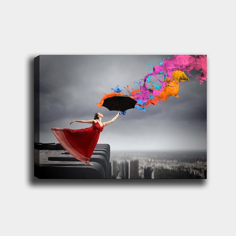 Canvastavla 70x100 cm - Kvinna i röd klänning står på en kant och håller ett paraply, medan färgglada färgstrålar sprutar ut från det, Röd / Svart / Orange