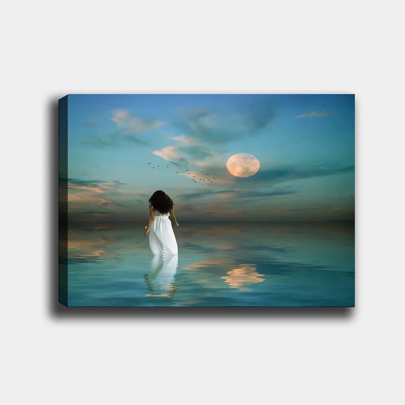 Canvastavla 70x100 cm - Kvinna i vit klänning går genom ett spegelblanka hav under en stjärnklar himmel med en stor måne, Blå / Vit / Grå