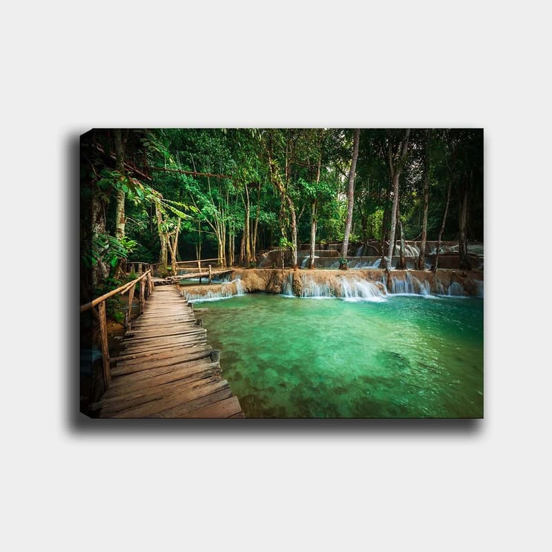 Canvastavla 70x100 cm - Lugn och naturskön plats med en träbro som leder över en klar, turkos vattenfallspool omgiven av frodig grönska - Turkos / Grön / Brun - Inredning - Tavlor & konst - Canvastavlor