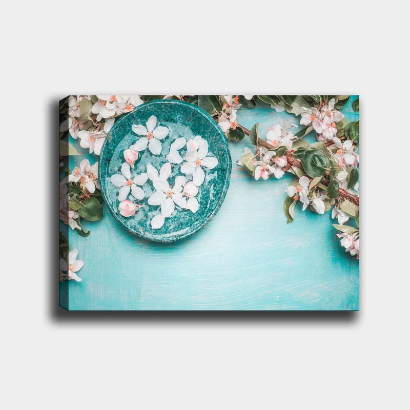 Canvastavla 70x100 cm - Skål med blommor omgiven av grönskande kvistar och blommor på en ljusblå bakgrund, Turkos / Vit / Rosa