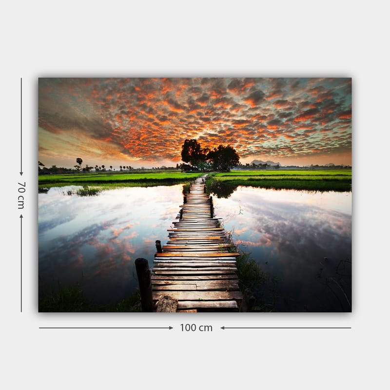 Canvastavla 70x100 cm - Träbro som sträcker sig över en spegelblanka vattenyta, omgiven av grönskande landskap och en dramatisk solnedgång - Orange / Grön / Blå - Inredning - Tavlor & konst - Canvastavlor