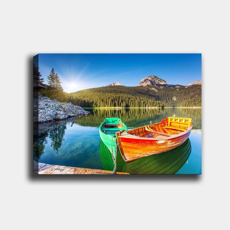 Canvastavla 70x100 cm - Två färgglada båtar ligger stilla vid en spegelblanka sjö omgiven av grönskande berg, Grön / Orange / Blå
