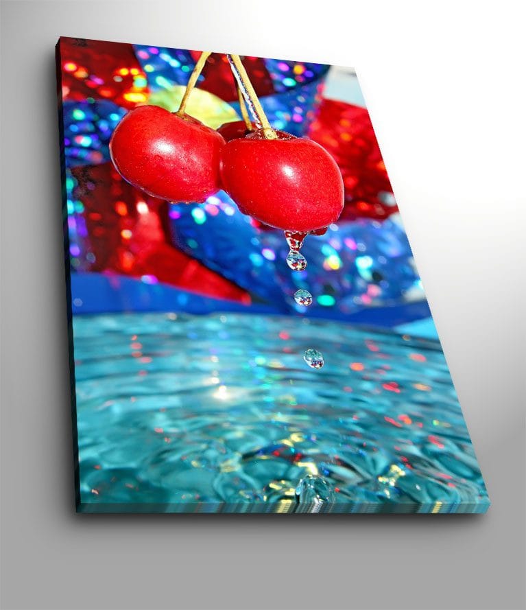 Canvastavla 70x100 cm - Två röda körsbär hänger över en vattenyta med droppar som faller ner, Röd / Blå / Turkos