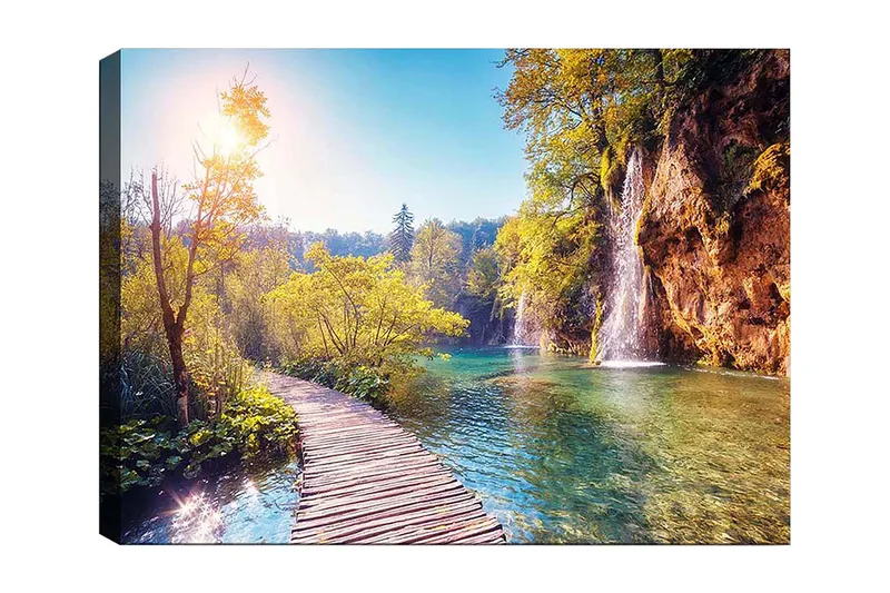 Canvastavla 70x100 cm - Vacker naturvy med en träbro som leder genom grönskande landskap och en vattenfall i bakgrunden, Grön / Blå / Gul