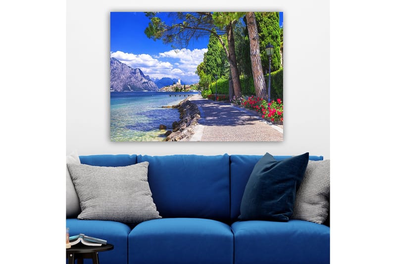 Canvastavla 70x100 cm - Vacker strandpromenad med träd och blommor vid en sjö, omgiven av berg och en pittoresk stad i bakgrunden - Blå / Grön / Röd - Inredning - Tavlor & konst - Canvastavlor