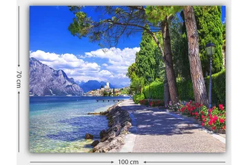 Canvastavla 70x100 cm - Vacker strandpromenad med träd och blommor vid en sjö, omgiven av berg och en pittoresk stad i bakgrunden - Blå / Grön / Röd - Inredning - Tavlor & konst - Canvastavlor
