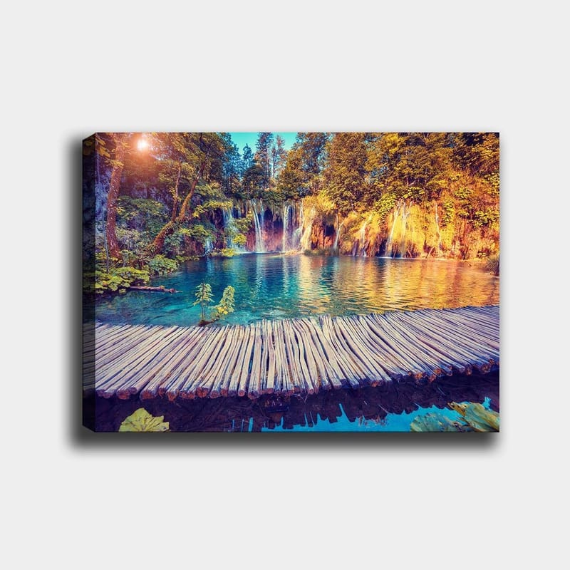 Canvastavla 70x100 cm - Vacker vattenfallsscen med klart blått vatten omgiven av frodig grönska och träd, Blå / Grön / Brun