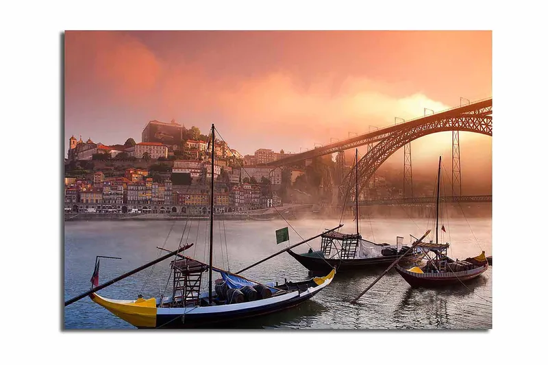 Canvastavla 70x100 cm - Vacker vy av floden med traditionella båtar och en majestätisk bro i bakgrunden, omgiven av färgglada hus, Orange / Blå / Gul