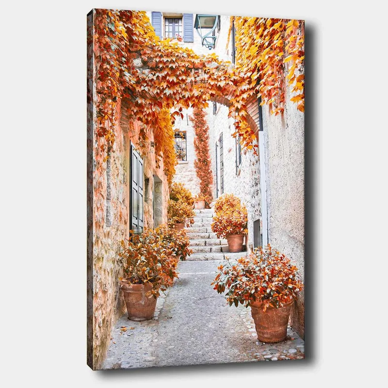 Canvastavla 70x100 cm - Pittoresk gränd omgiven av färgglada höstlöv och krukväxter, Orange / Brunt / Gult
