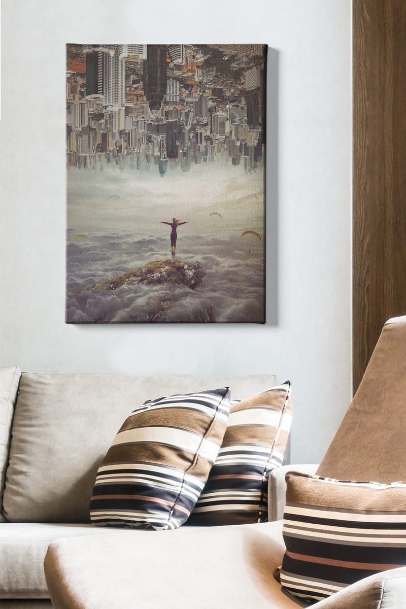 Canvastavla 70x100 cm - Person står med utsträckta armar på en klippa ovanför molnen, med en stad i bakgrunden som är upp och ner - Grå / Beige / Mörkblå - Inredning - Tavlor & konst - Canvastavlor