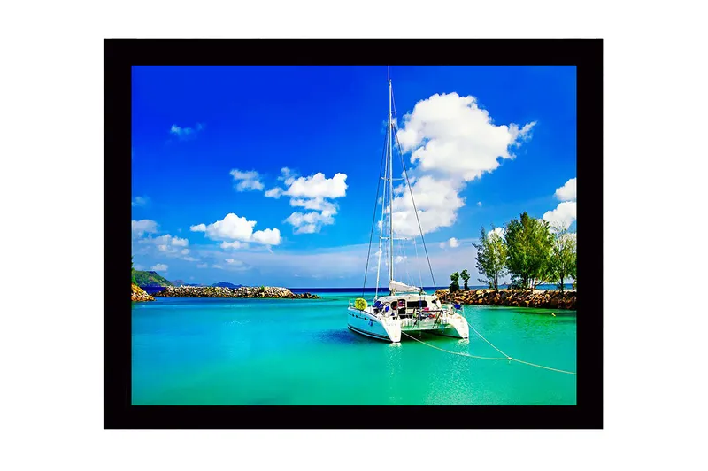 Inramad Canvastavla i trä - 41x56 cm - Segelbåt i en klar, turkos lagun under en blå himmel med vita moln, Turkos / Blå / Vit